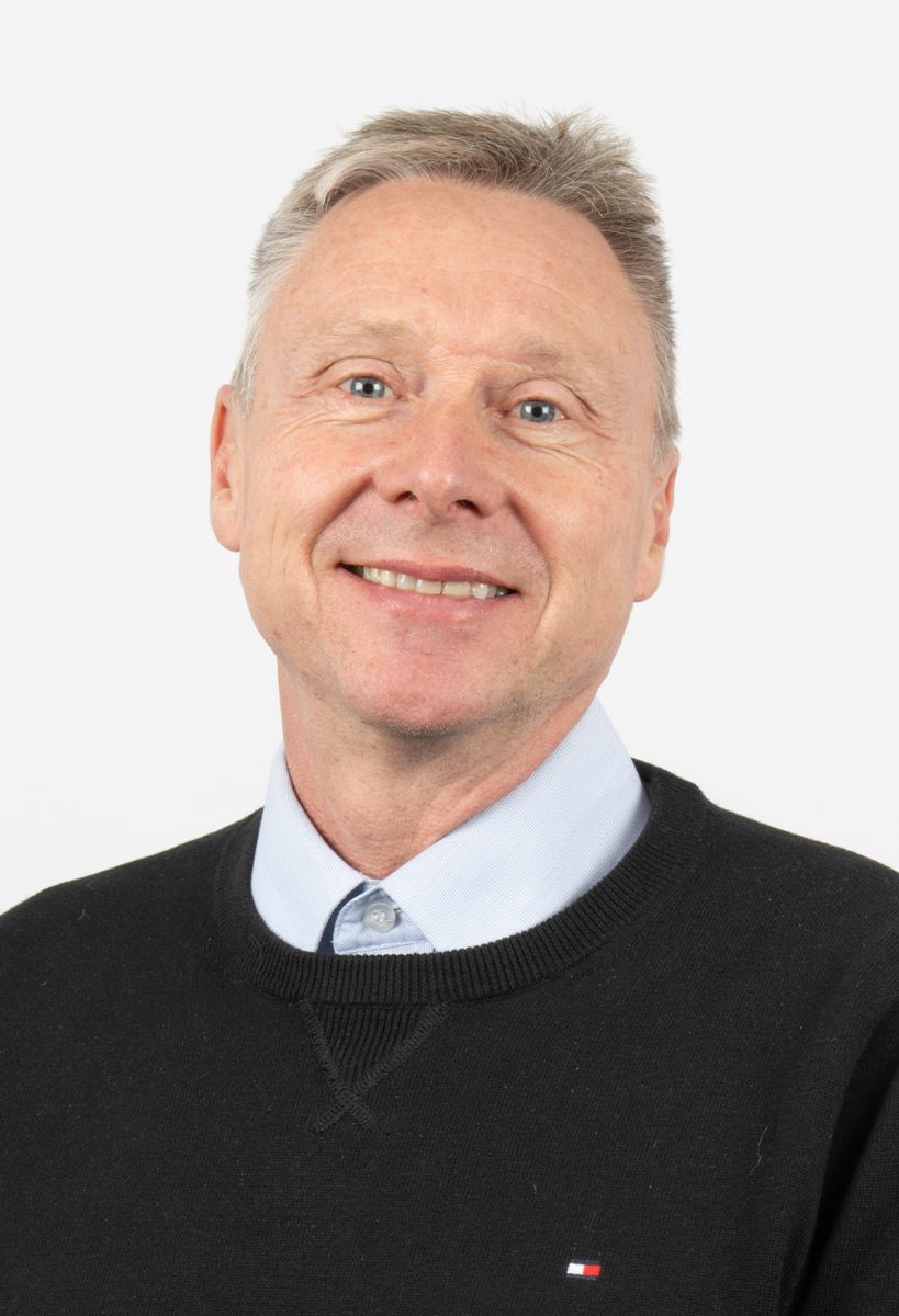 Smiling Keith Watson from DIS Consulting IT wearing a black sweater over a light blue shirt, standing against a plain light background.
